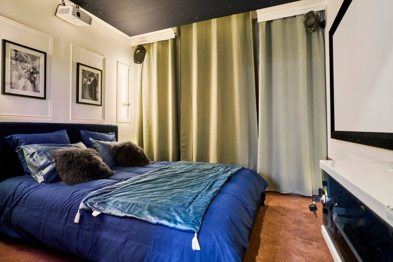 A bedroom with a bed, curtains, a projector, and framed pictures on the wall.