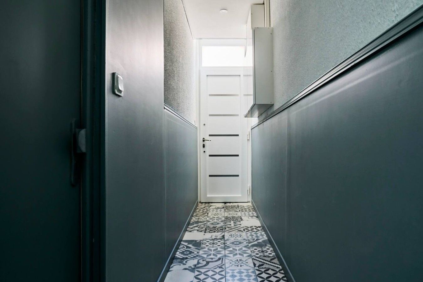 A narrow hallway with a patterned tile floor leading to a door.