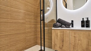 A modern bathroom with wooden paneling, a round mirror, a white vanity, and toiletries. - Vrbo Property (Armentières)
