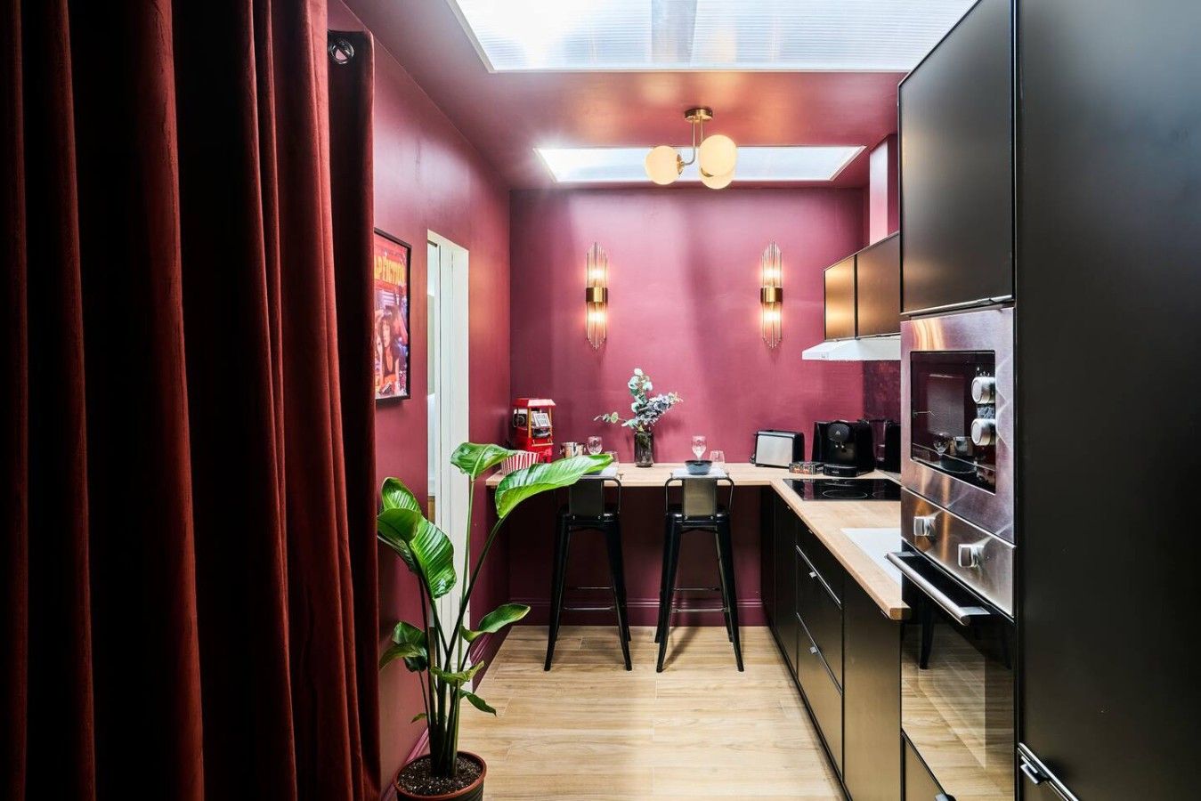 Una cucina compatta dal design moderno, con un piano di lavoro, sgabelli da bar, una macchina da caffè e un forno a incasso.