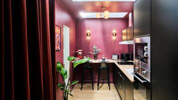 Una cucina compatta dal design moderno, con un piano di lavoro, sgabelli da bar, una macchina da caffè e un forno a incasso.