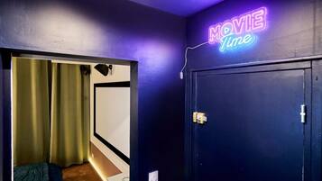 A room with a neon sign reading 'MOVIE Time' on the wall, a door with a handle, and a partial view of a bed with a blanket.
