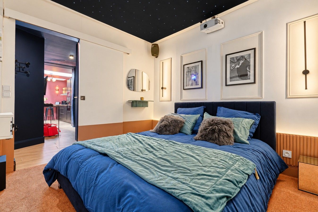 A bedroom with a bed, a nightstand, a projector, and framed pictures on the wall.