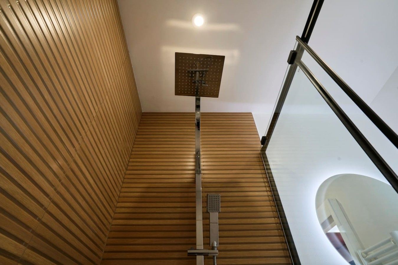 Een moderne badkamer met een houten vloer, een douche met bedieningspaneel en een glazen balustrade.