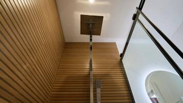 Een moderne badkamer met een houten vloer, een douche met bedieningspaneel en een glazen balustrade.