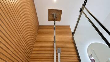 A modern bathroom with a wooden slatted wall, a shower with a square showerhead, and a glass railing.