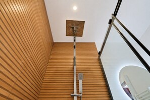 A modern bathroom with a wooden slatted wall, a shower with a square showerhead, and a glass railing.