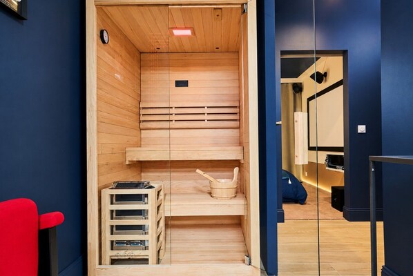 A sauna room with wooden benches, a clock, and a small table with items.