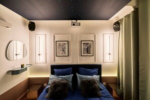 Ein Schlafzimmer mit Sternenhimmel, gerahmten Bildern an der Wand, einem Bett mit blauer Bettwäsche und einem Nachttisch.
