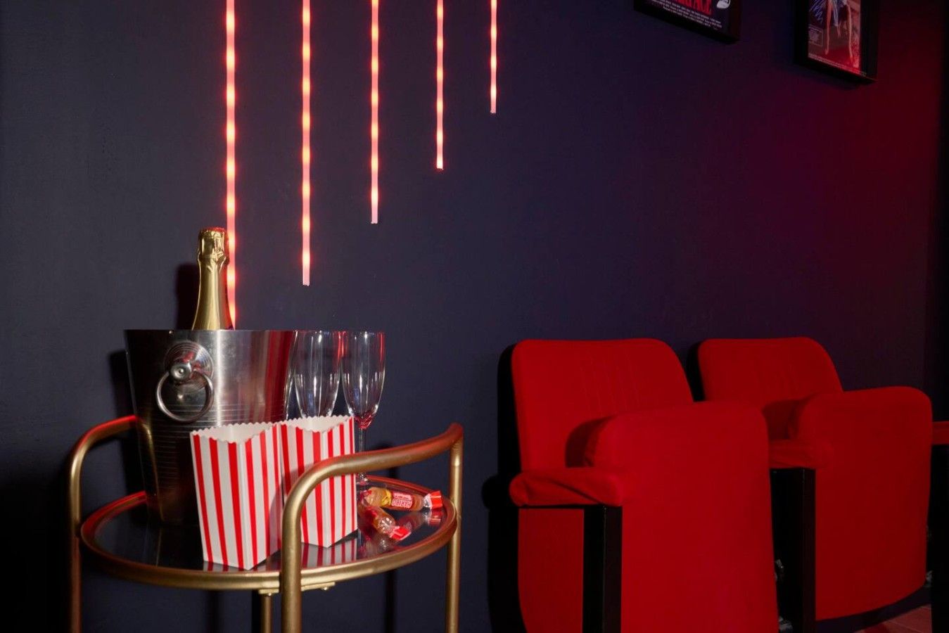 Une pièce comprenant un fauteuil rouge de style cinéma, une petite table avec un récipient à pop-corn et une bouteille de champagne.