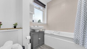 A modern bathroom with a bathtub, a sink, and a toilet. - Arcade Machine | Games | Large House | Sleeps 6 (Coventry)