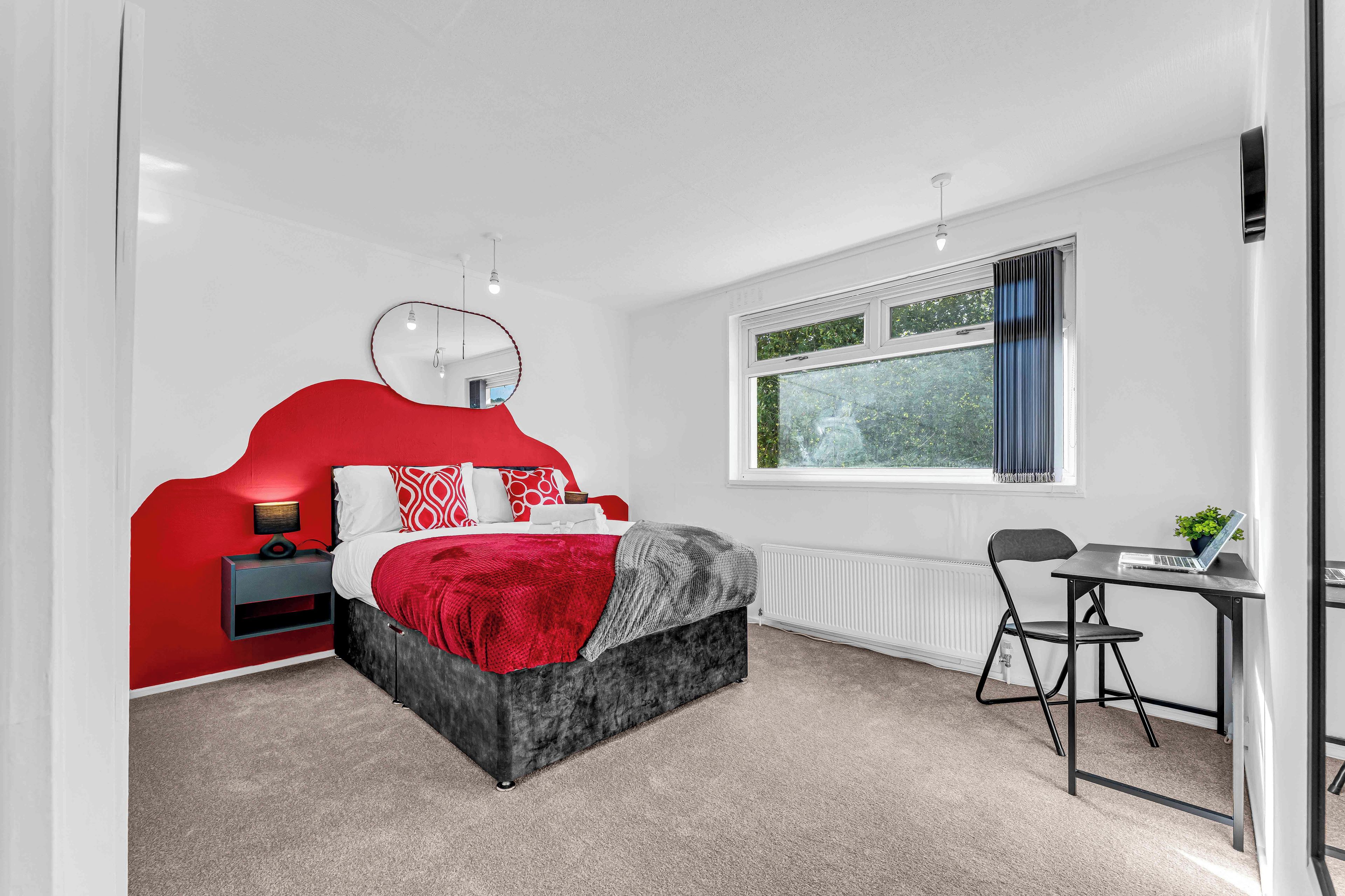 A modern bedroom with a bed, bedside table, and a desk with a chair.