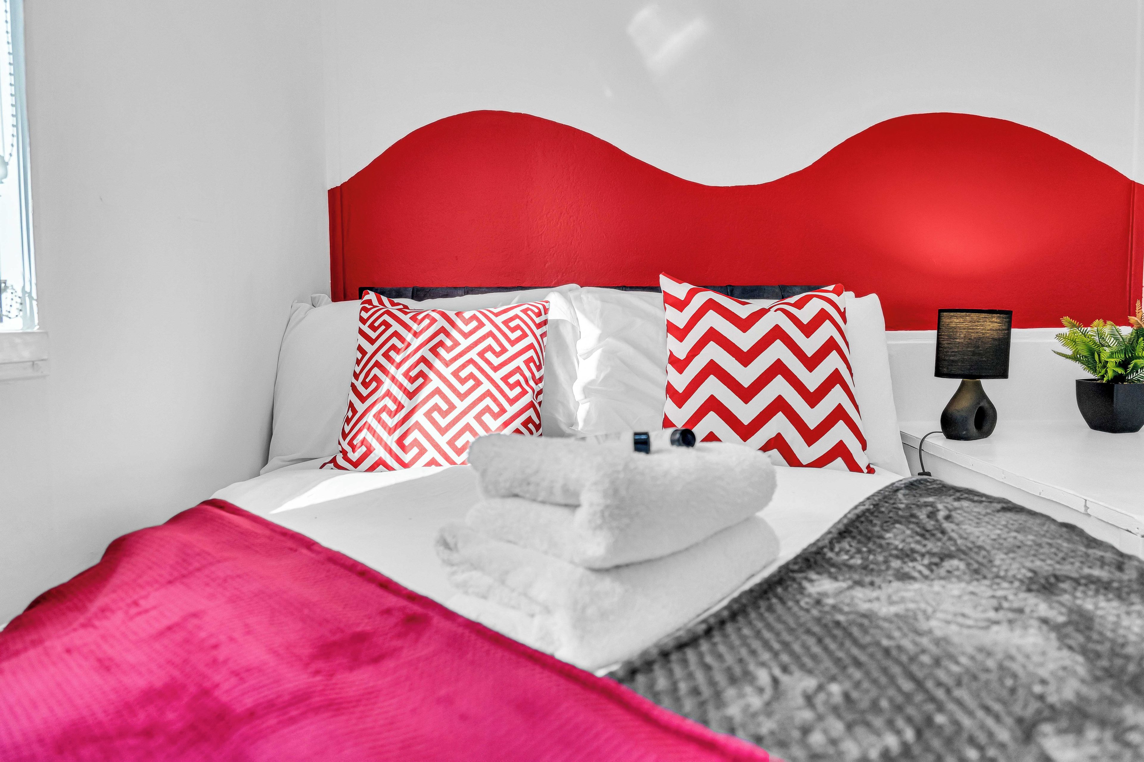 Una cama con cabecera roja, ropa de cama blanca y dos almohadas estampadas.