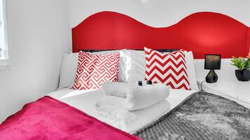 Una cama con cabecera roja, ropa de cama blanca y dos almohadas estampadas.
