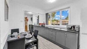 A modern kitchen with grey cabinets, a dining table set for four, and a large window with a view of the outside. - Arcade Machine | Games | Large House | Sleeps 6 (Coventry)