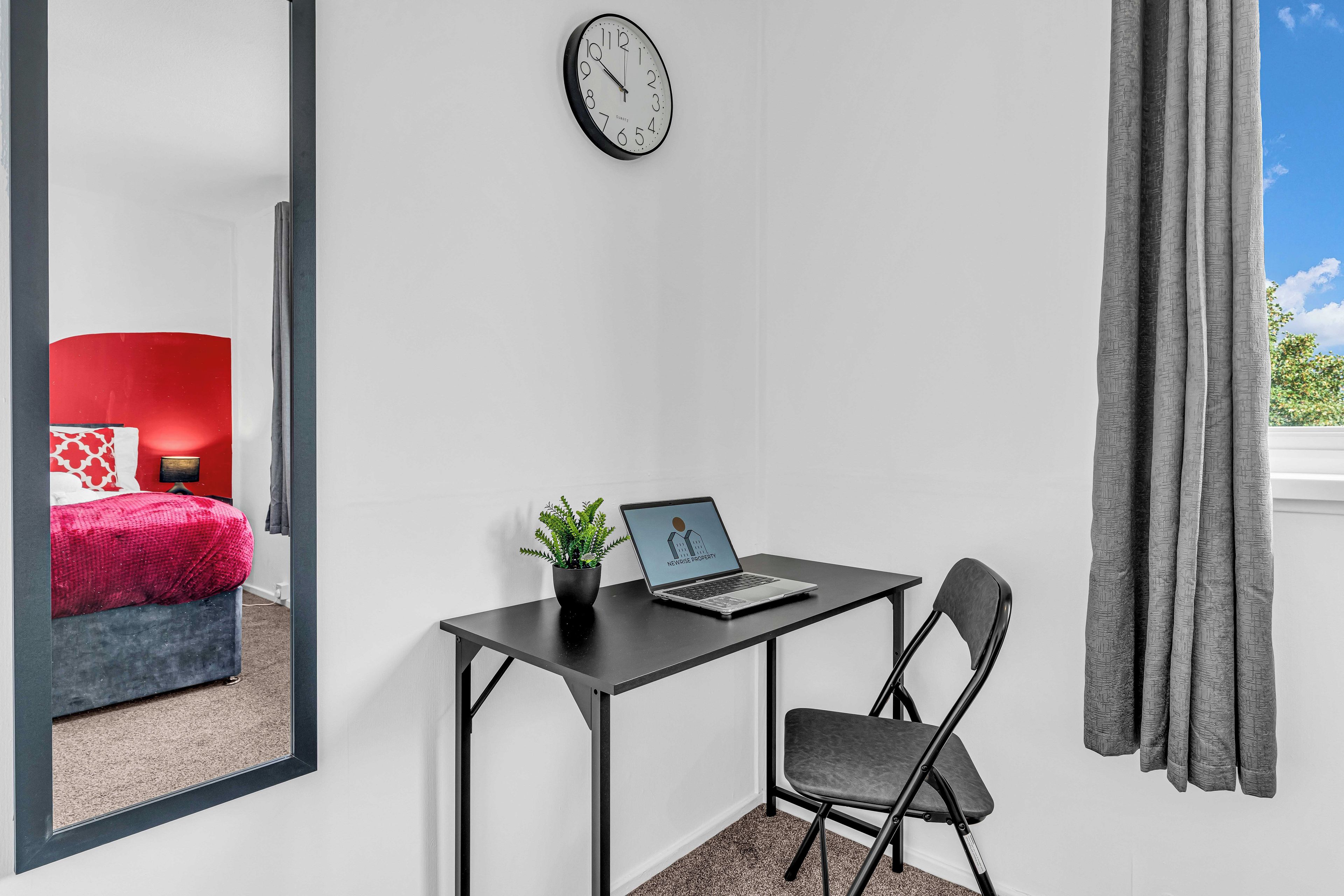 A room with a desk, chair, laptop, and a clock on the wall.