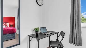 A room with a desk, chair, laptop, and a clock on the wall.
