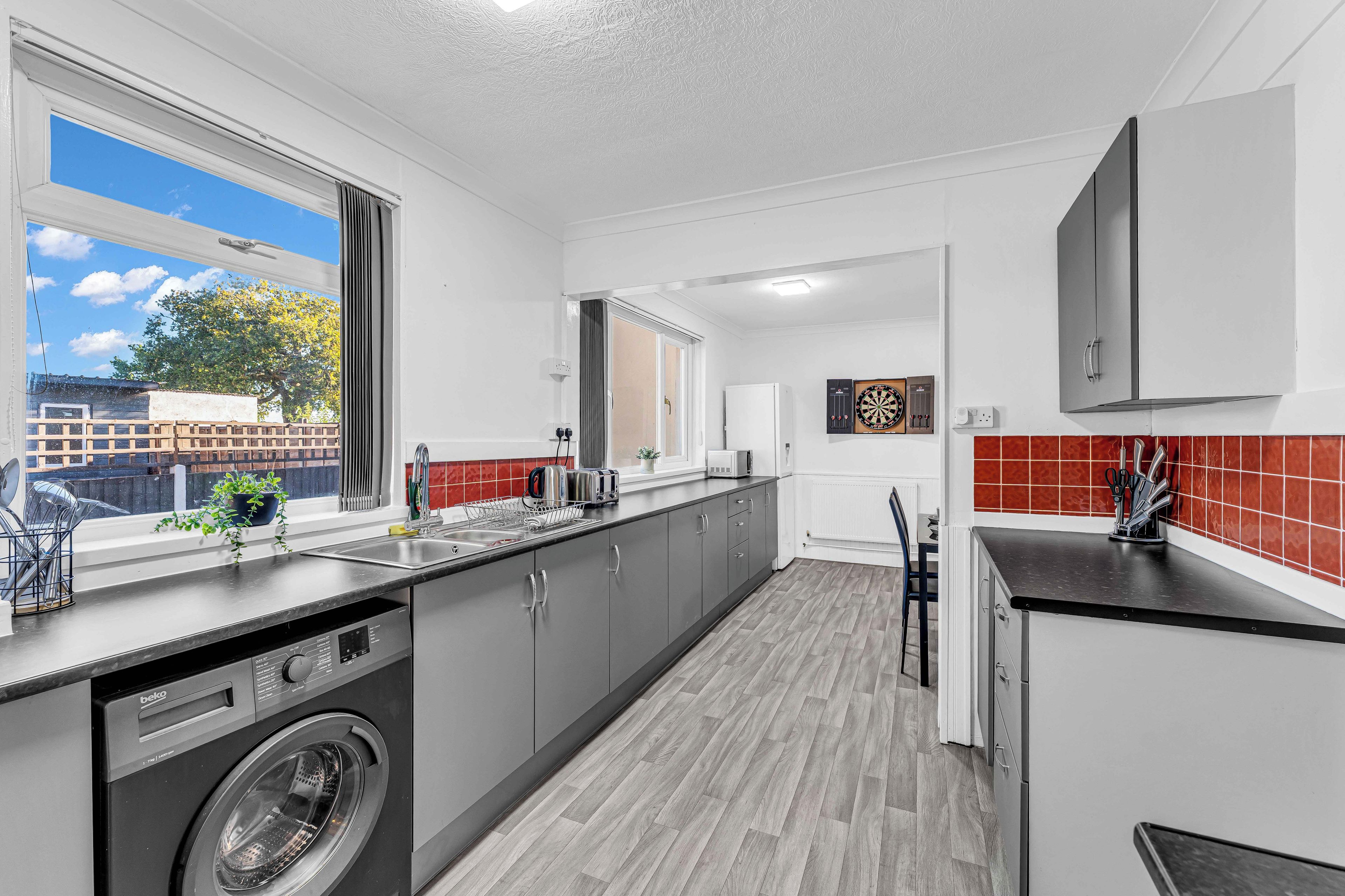 Una cocina moderna con armarios grises, lavadora integrada y ventana con vistas al exterior.