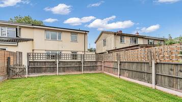 A residential backyard with a grassy lawn, a wooden fence, and two houses with visible windows and doors.