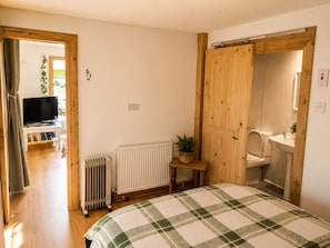 Ein Schlafzimmer mit Bett, Heizkörper, Fernseher und einem durchgegangenen Tür sichtbaren Badezimmer.