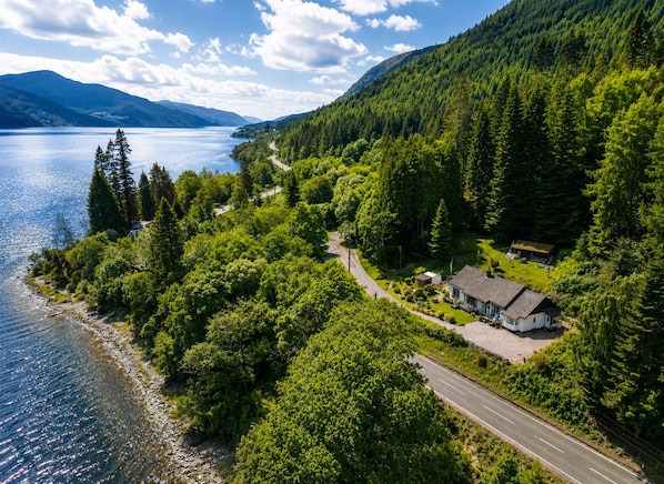 Ein Haus am See mit einer Straße und dichtem Wald.