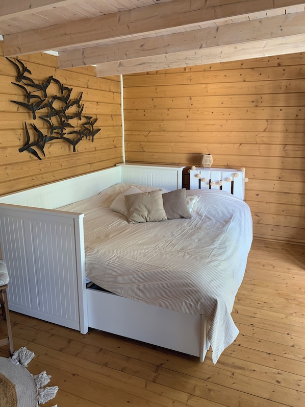 A bed with a white frame and beige bedding in a room with wooden walls and a sloped ceiling.