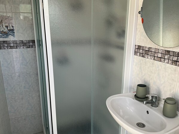A bathroom with a glass shower enclosure, a white sink with a mirror above it, and a tiled backsplash.