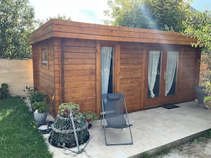 A wooden cabin with a patio, a chair, and potted plants.