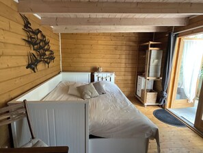 Ett rum med träpanel, en säng, ett element, en hylla och en dörr som leder ut.