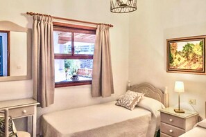 Ein Schlafzimmer mit Bett, Nachttisch, Lampe, einem Fenster mit Vorhängen und einem Bild an der Wand.