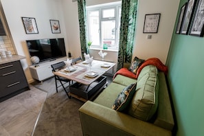 Ein modernes Wohnzimmer mit Essbereich, einem Flachbildfernseher und einer Couch mit Kissen.