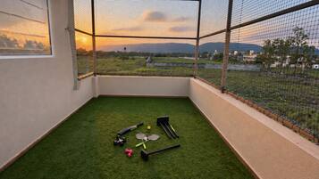 A room with a view of a field and mountains, containing exercise equipment like dumbbells and a yoga mat.