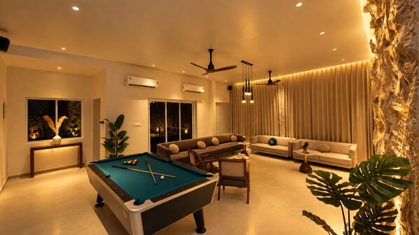 A modern living room with a pool table, sofas, and a dining area.