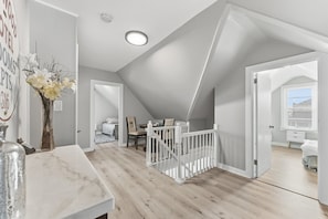 A spacious attic bedroom with a sloped ceiling, a white railing, and a view of the sky through a window. - Spacious 6BR Retreat Steps from Beach & Boardwalk (Wildwood Crest)