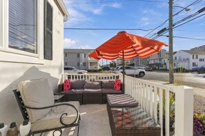 A balcony with a wicker sofa, a small table, and an orange-striped umbrella. - Spacious 6BR Retreat Steps from Beach & Boardwalk (Wildwood Crest)