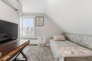 Une chambre à coucher comprenant un lit, un bureau, une chaise, un radiateur, une fenêtre avec des stores et un tableau encadré accroché au mur.