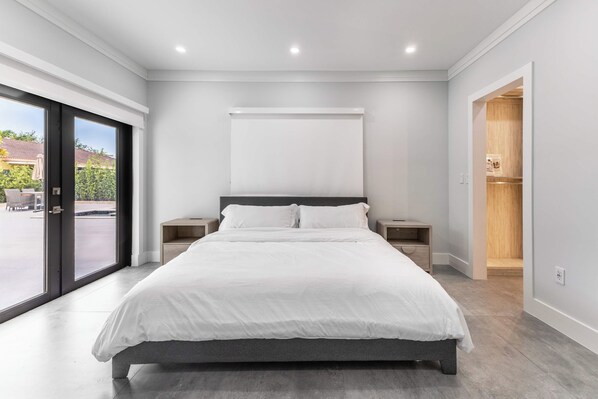 A modern bedroom with a large bed, two bedside tables, a wardrobe, and a sliding glass door to a balcony.