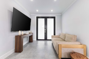 A modern living room with a flat-screen TV, a wooden console table, a beige sofa, and a large glass door leading to an outdoor area. - Homestead Keys Gateway - Private Pool & Gym (Homestead)