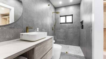 A modern bathroom with a large sink, vanity, and shower area.