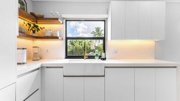 A modern kitchen with white cabinetry, a built-in window, and a countertop with a blender and jars.