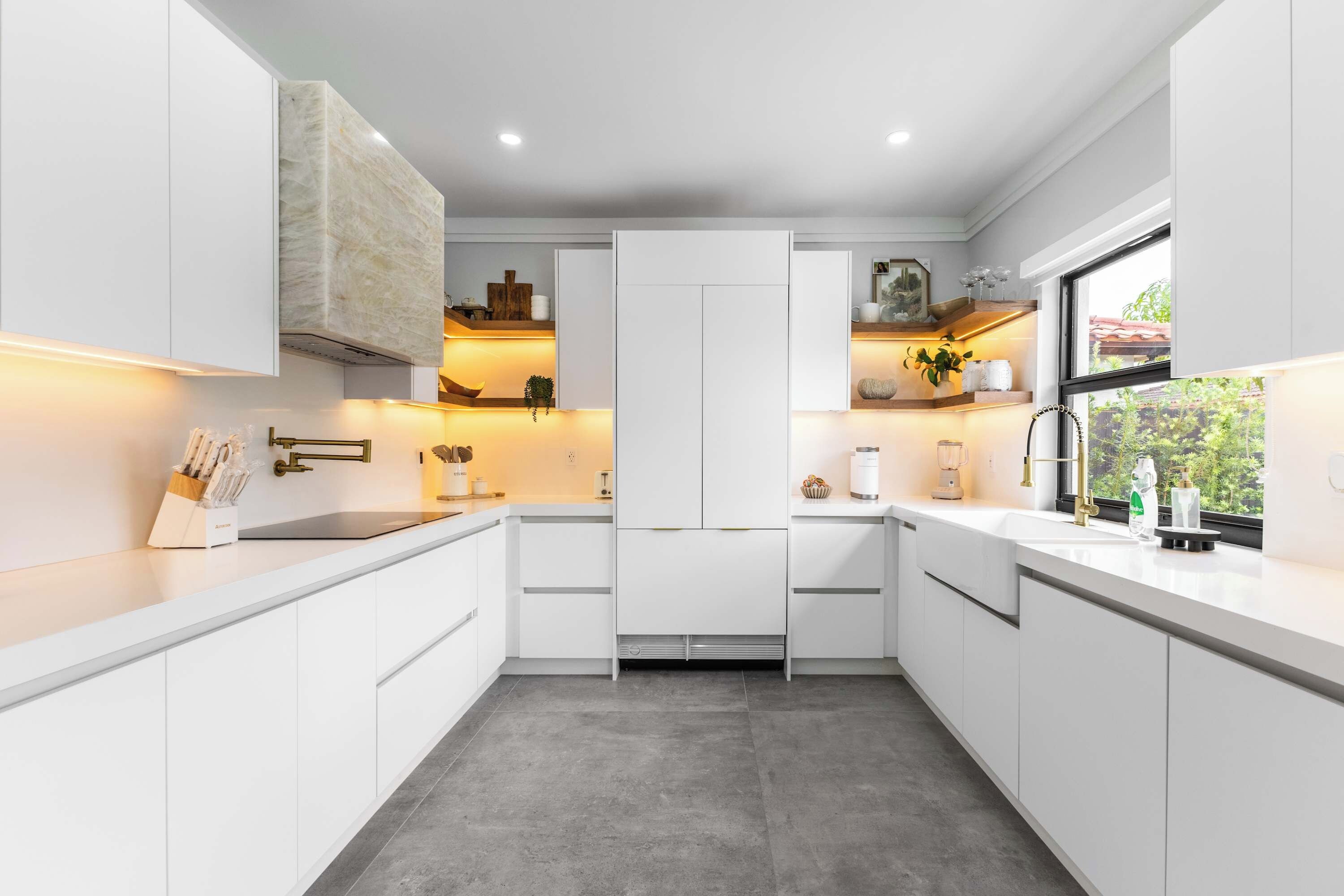 A modern kitchen with white cabinetry, a built-in oven, and a window providing a view of greenery outside.