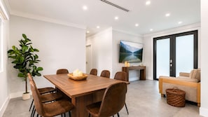 A modern living room with a wooden dining table, comfortable seating, a large flat-screen TV, and a cozy sofa.