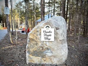 En stor sten med et skilt der siger 'Chandler Heights Village' i et skovområde, hvor der kan ses et 'ONE WAY' skilt i baggrunden.