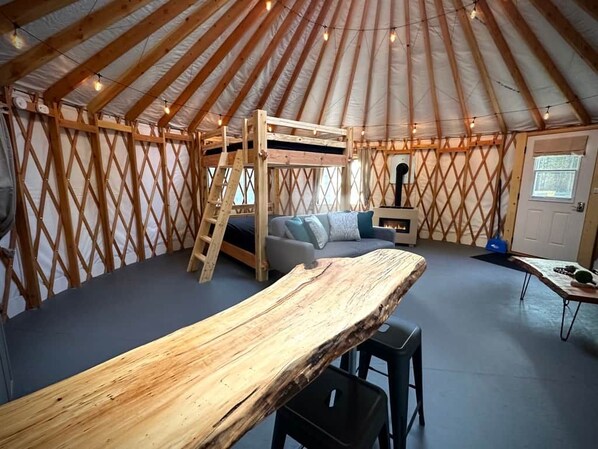 A yurt interior with a bunk bed, a sofa, a dining table, and a fireplace.