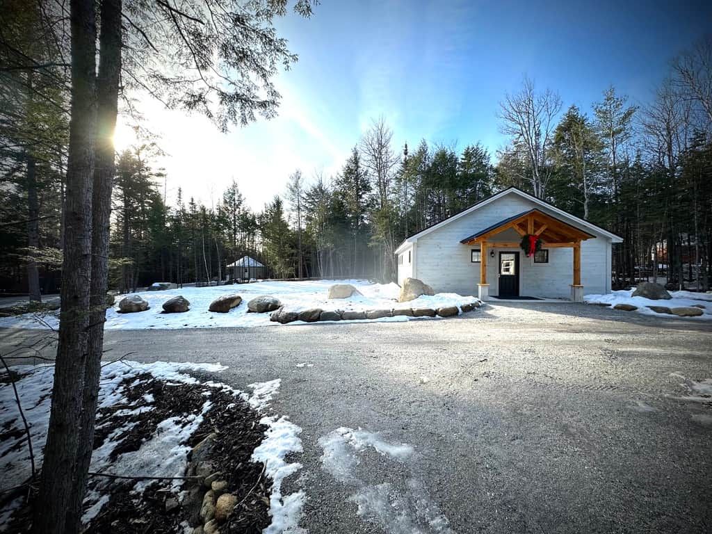 A cabin with a wooden porch, surrounded by snow-covered ground and trees.