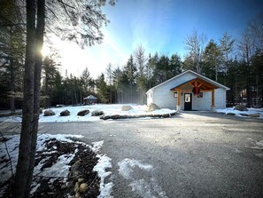 En hytte med en træterrasse, omgivet af sneklædt jord og træer.