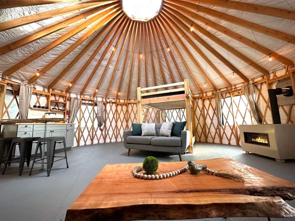 A yurt interior with a central seating area, a kitchenette, and a fireplace.