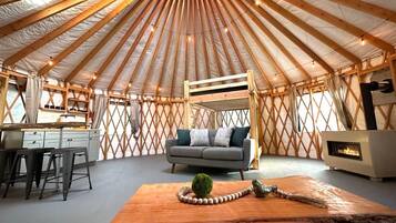 A yurt interior with a central seating area, a kitchenette, and a fireplace.