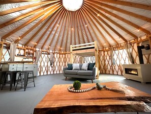 Et yurt-interiør med et centralt siddeområde, et tekøkken og en pejs.