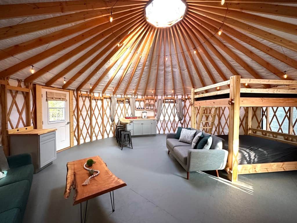 En inredning i en jurta med ett centralt träpanelat tak, en soffa, en matplats och en våningssäng.